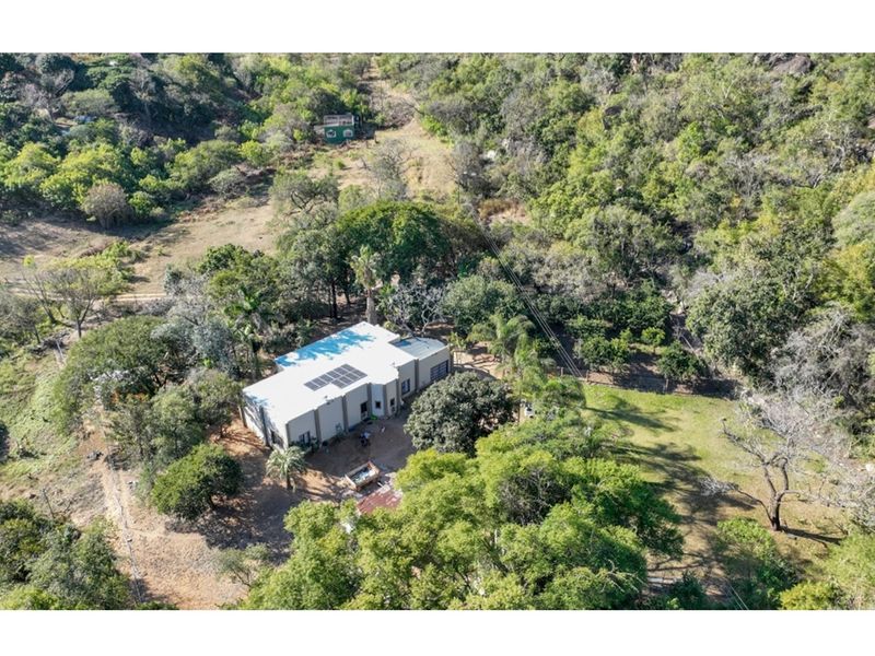 Aerial view of a farm property featuring a main dwelling with solar panels, surrounded by extensive natural vegetation and mature trees.