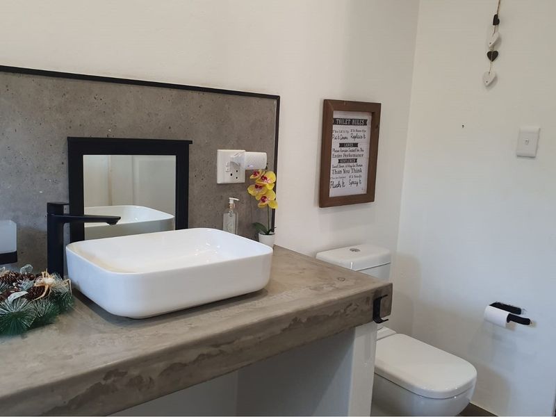 A modern bathroom featuring a concrete vanity countertop, a contemporary vessel sink with black faucet, and a white toilet.