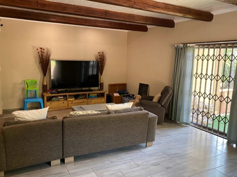 Spacious living room featuring exposed timber ceiling beams, tiled flooring, and a sliding glass door with security gate leading to the exterior.