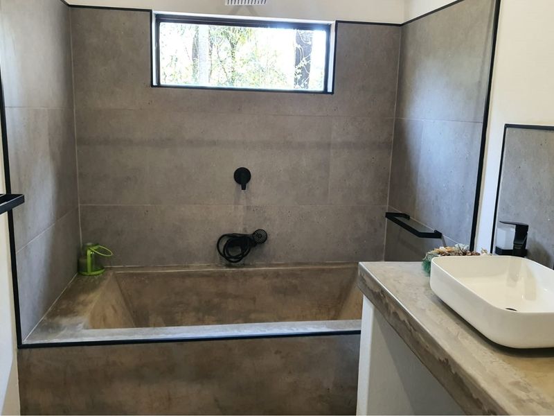 Modern bathroom featuring a built-in concrete bathtub, sleek grey wall tiling, black matte fixtures, and a contemporary vessel sink on a concrete vanity.