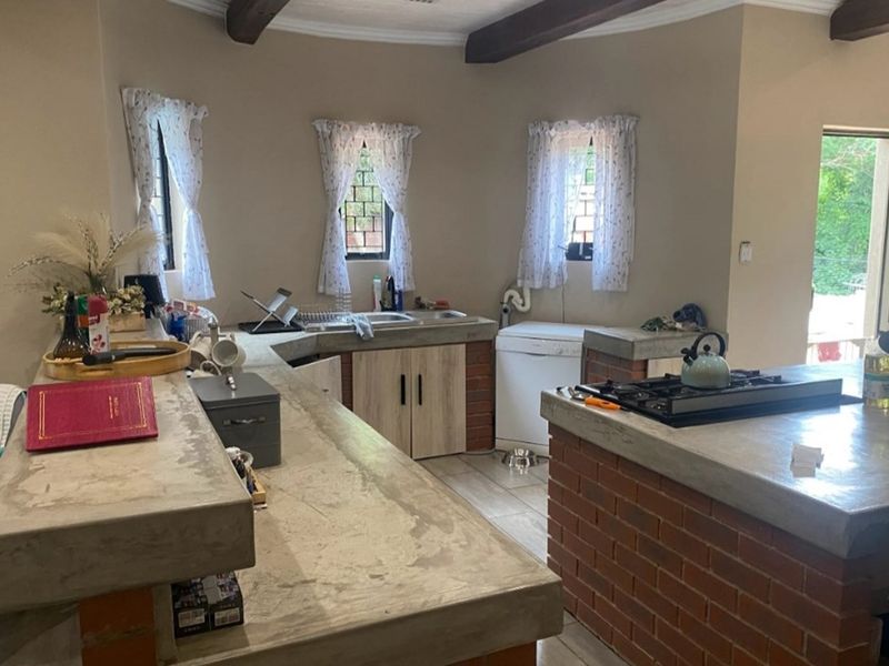 Rustic kitchen featuring custom concrete countertops, exposed brick base cabinetry, built-in gas hob, and tiled flooring with exposed ceiling beams.