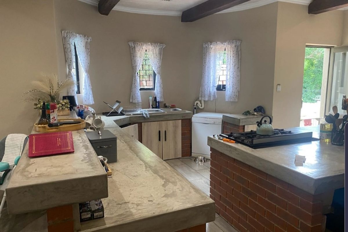 Rustic kitchen featuring custom concrete countertops, exposed brick base cabinetry, built-in gas hob, and tiled flooring with exposed ceiling beams.
