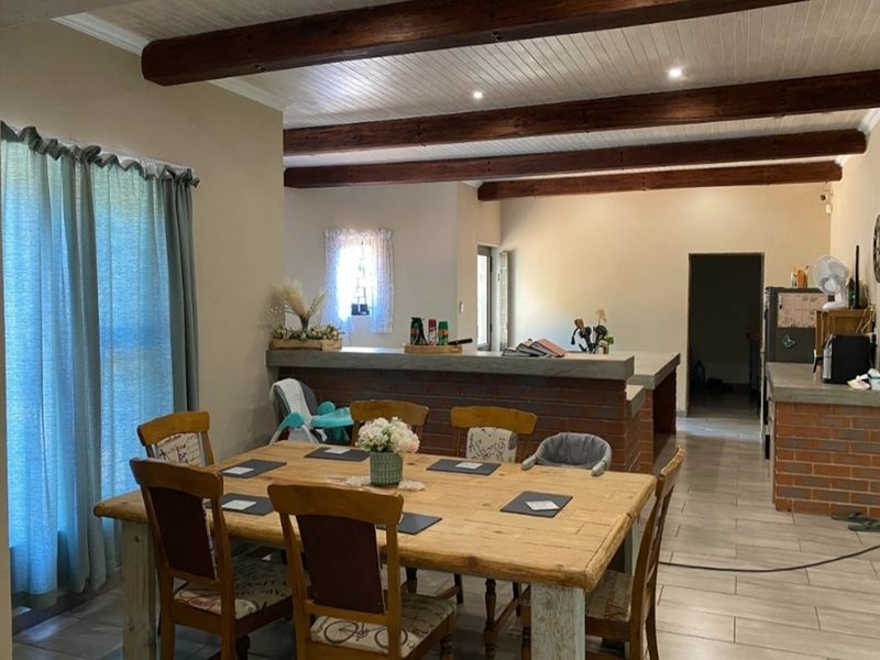 Open plan living and dining area featuring exposed timber ceiling beams, brick breakfast bar, and tiled flooring.