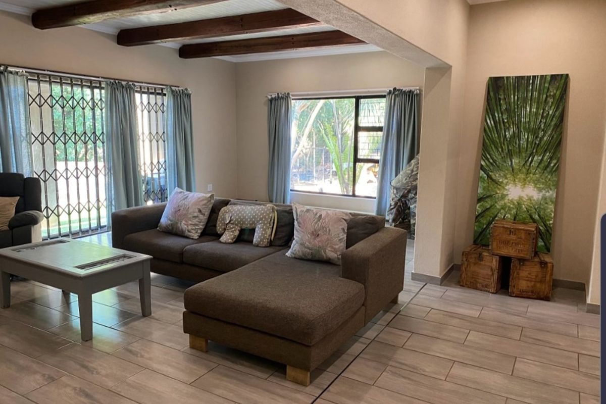 Spacious living area featuring exposed timber ceiling beams and large windows, providing a bright and inviting atmosphere with tiled flooring throughout.