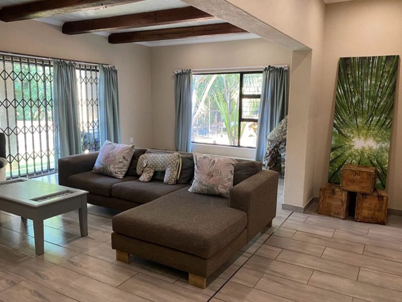 Spacious living area featuring exposed timber ceiling beams and large windows, providing a bright and inviting atmosphere with tiled flooring throughout.