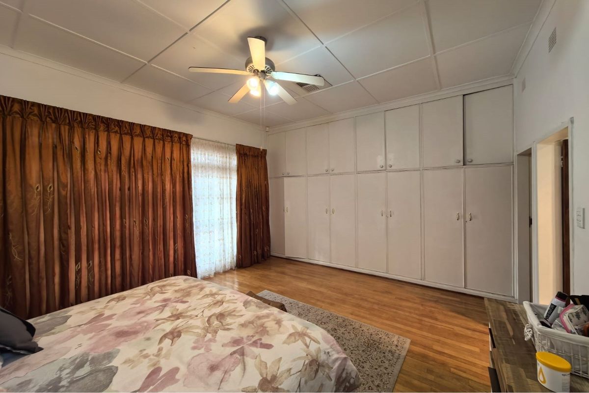 Spacious bedroom featuring extensive wall-to-wall built-in cupboards, timber flooring, and a ceiling fan, offering ample storage and a classic layout.