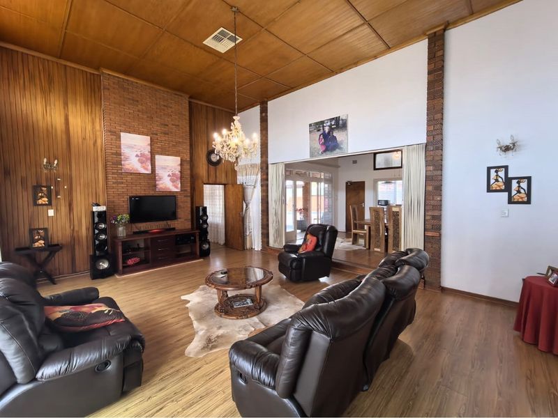 Spacious living room featuring a high timber ceiling, exposed brick accent wall, and warm timber-look flooring, creating a classic and inviting atmosphere.
