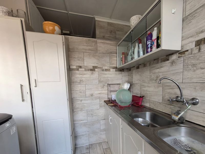 A functional laundry area featuring a stainless steel double sink, wall-mounted tap, and ample built-in cabinetry with tiled wall finishes.