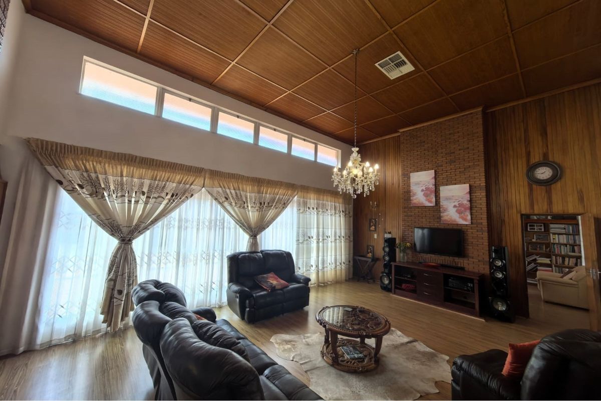 Spacious living room featuring a high timber panelled ceiling, exposed brick feature wall, and large windows with natural light.