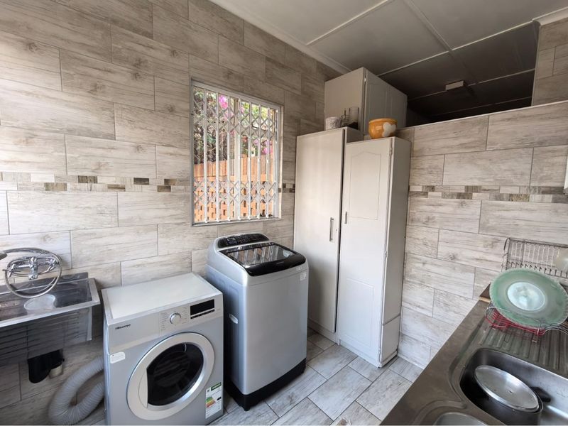 A functional laundry area featuring tiled walls, built-in cabinetry, and a stainless steel sink, providing practical utility space for household tasks.