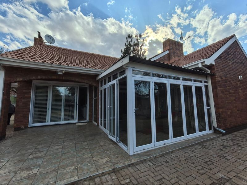 Rear view of the property featuring a brick facade, tiled roof, and a modern enclosed patio with bi-fold glass doors and tiled flooring.