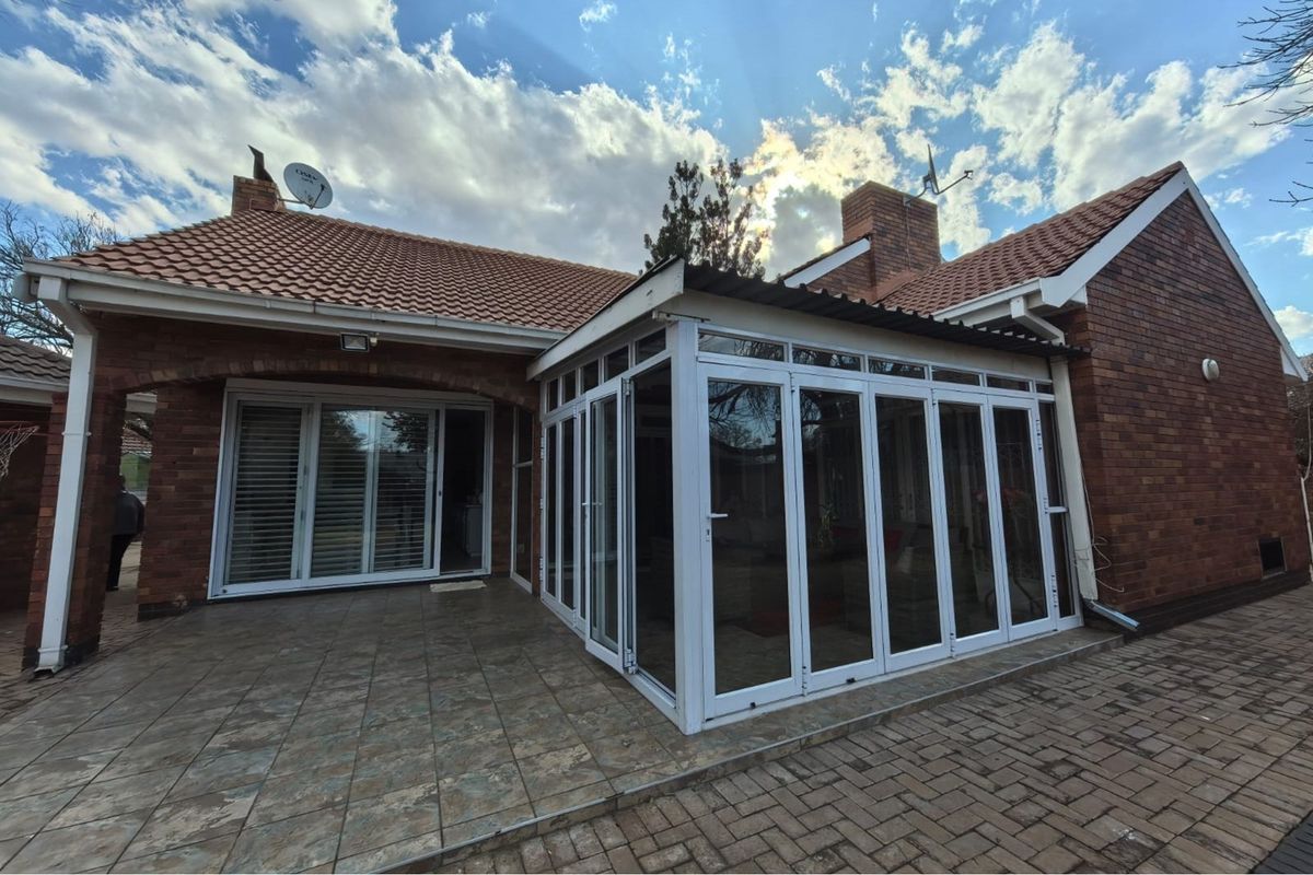 Rear view of the property featuring a brick facade, tiled roof, and a modern enclosed patio with bi-fold glass doors and tiled flooring.