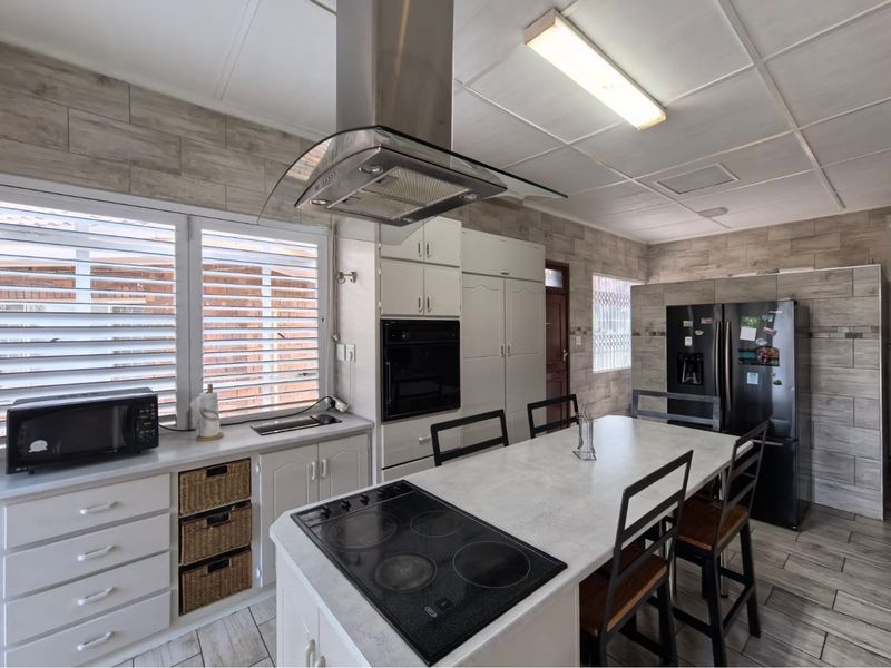 A functional kitchen featuring a central island with an integrated electric hob, extractor fan, built-in oven, and ample cabinetry with tiled wall finishes.