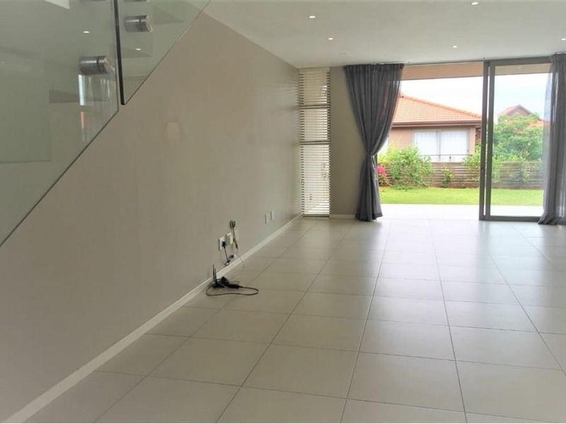Spacious open-plan living area featuring large format floor tiles, a glass-panelled staircase, and sliding doors leading to a private garden patio.