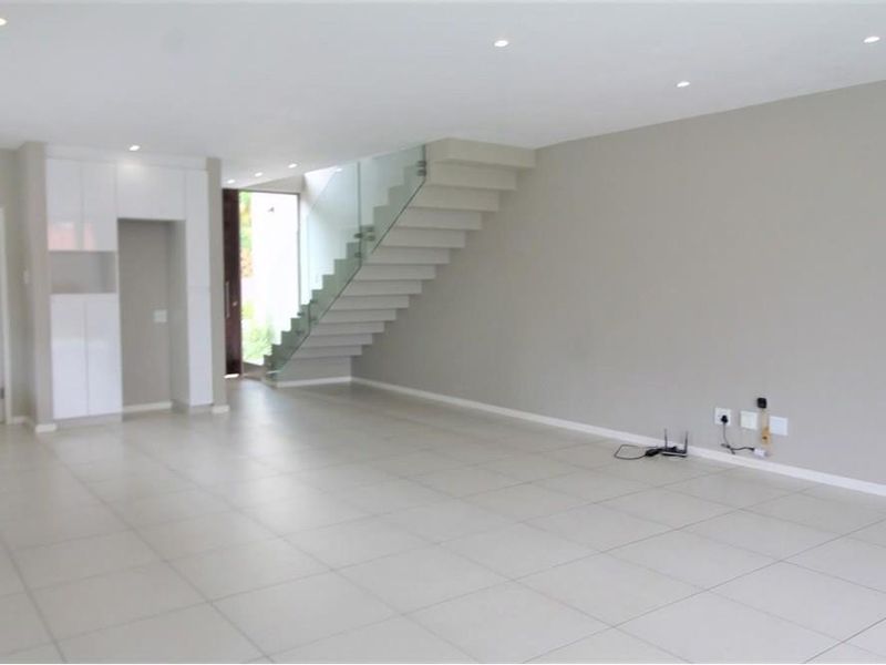 Spacious open-plan living area featuring modern tiled flooring, recessed ceiling lighting, and a contemporary staircase with a glass balustrade.