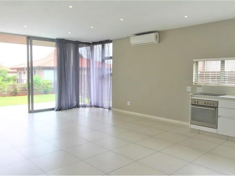 Spacious open-plan living area featuring tiled flooring, recessed lighting, a wall-mounted air conditioning unit, and a compact kitchen with a built-in oven and hob.