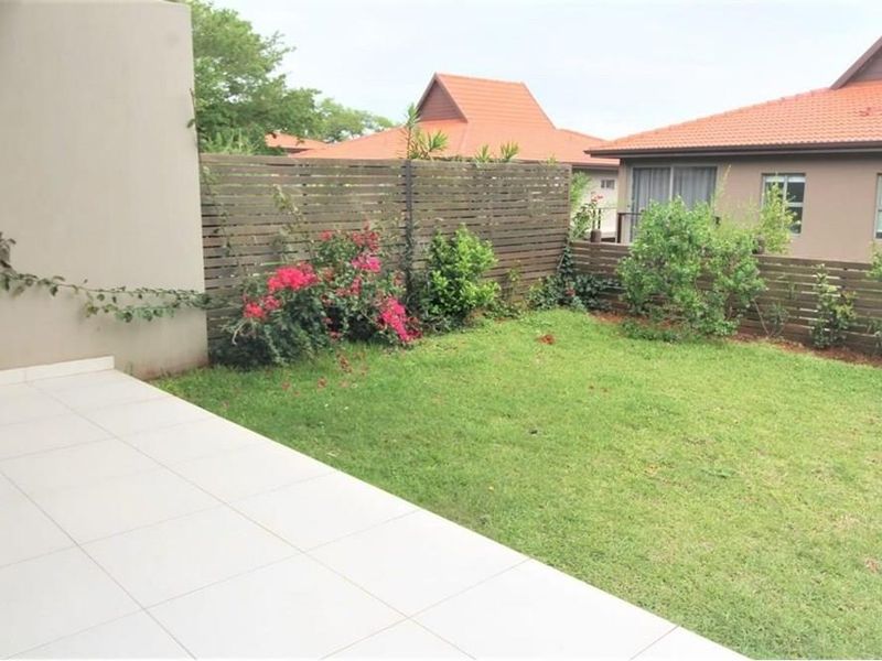 A private rear garden featuring a tiled patio area, established lawn, and timber boundary fencing, providing a pleasant outdoor space for the townhouse.