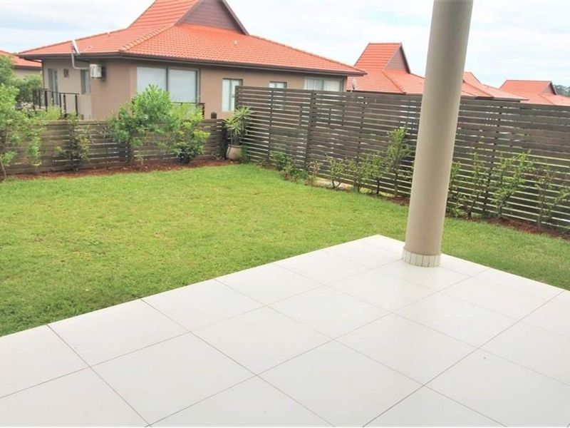 A private rear garden featuring a tiled patio area, a well-maintained lawn, and timber slat privacy fencing.