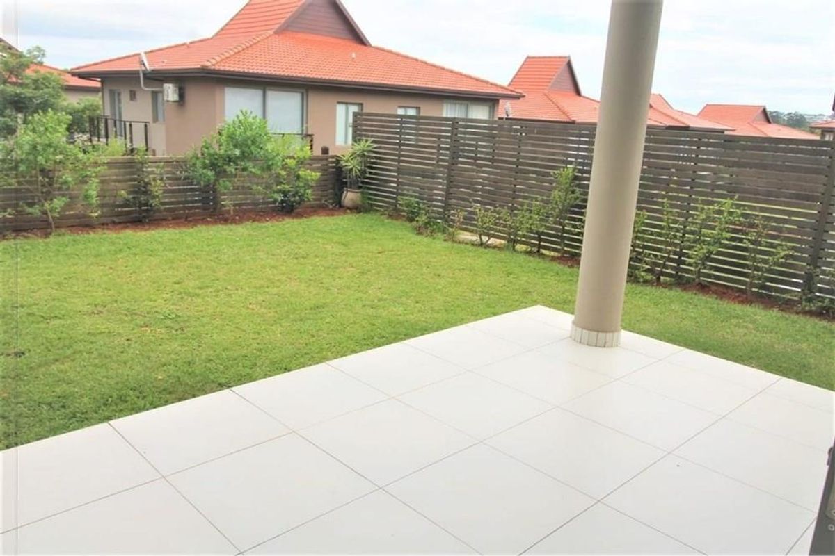 A private rear garden featuring a tiled patio area, a well-maintained lawn, and timber slat privacy fencing.