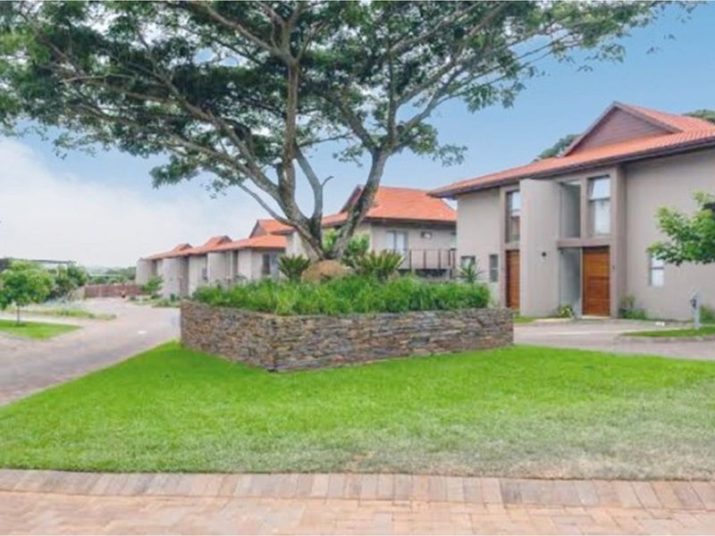 A view of the townhouse complex exterior featuring landscaped gardens, paved driveways, and well-maintained residential units with tiled roofs.