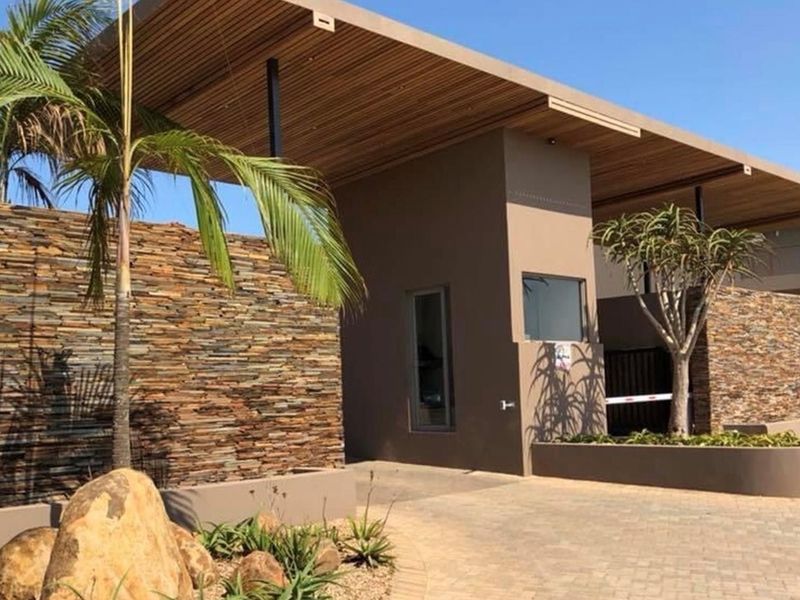 Modern gated estate entrance featuring stone cladding, timber-slatted roof overhang, and paved driveway access.