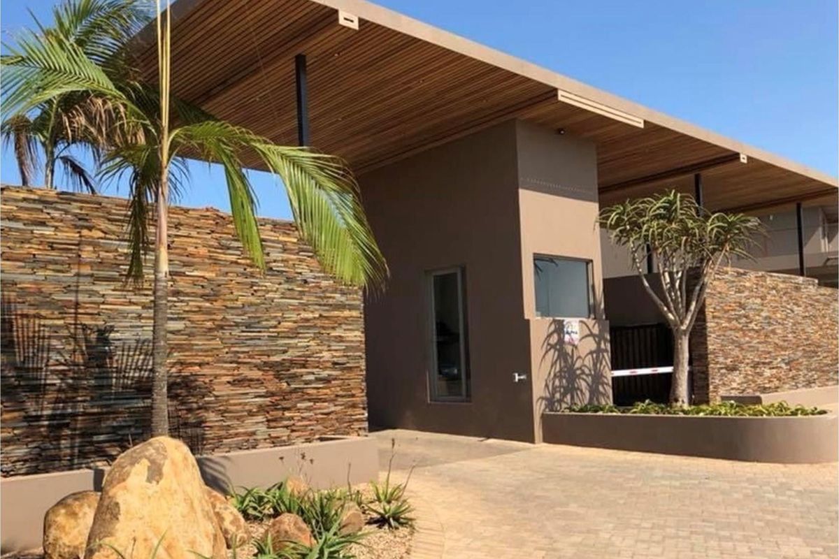 Modern gated estate entrance featuring stone cladding, timber-slatted roof overhang, and paved driveway access.