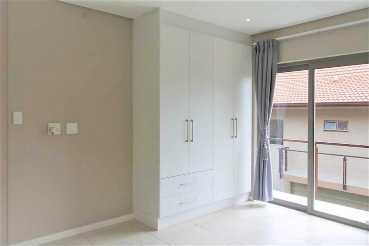 A bright bedroom featuring built-in white cabinetry, tiled flooring, and sliding glass doors that open to a balcony.