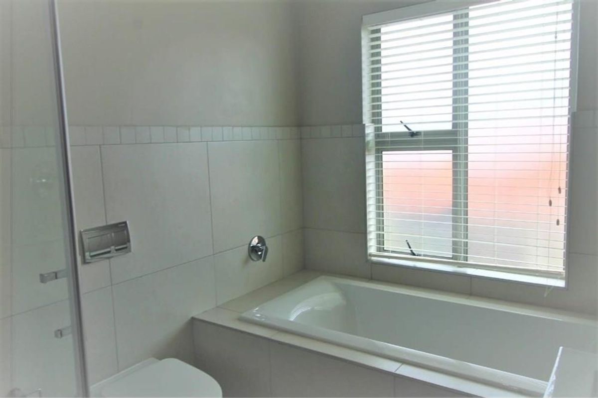 A functional bathroom featuring a built-in bathtub, tiled walls, and a window with fitted blinds.