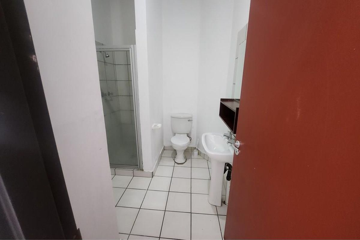 A functional bathroom featuring a pedestal sink, a standard toilet, and a glass-enclosed shower stall with tiled flooring.