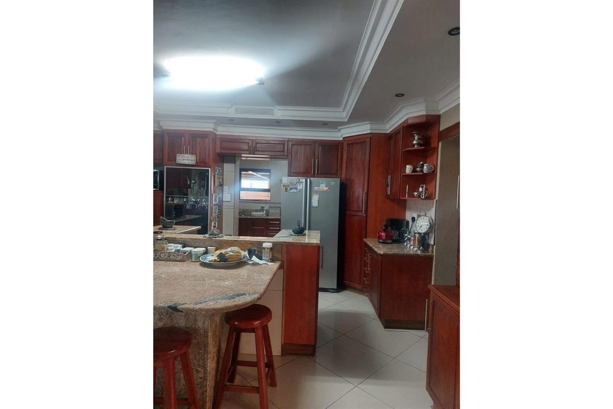 A traditional kitchen featuring rich wood cabinetry, granite countertops, a breakfast bar, and tiled flooring with recessed ceiling lighting.