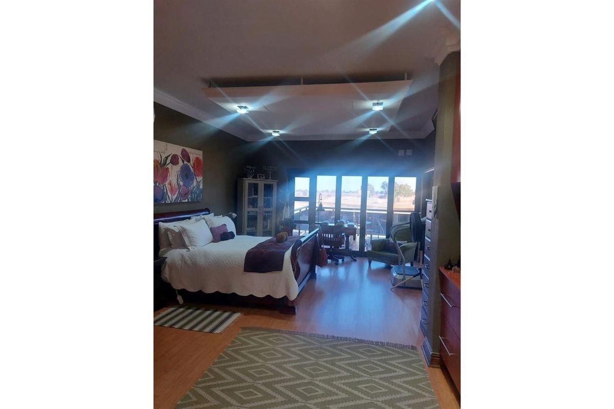 Spacious bedroom featuring laminate flooring, a recessed tray ceiling with integrated downlights, and large glass sliding doors opening to an outdoor area.