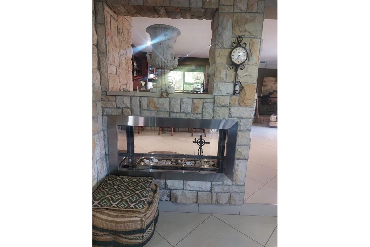 A feature stone-clad double-sided fireplace with a modern stainless steel insert, serving as a central room divider in an open-plan living area.