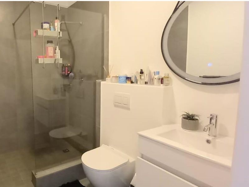 Modern bathroom featuring a walk-in shower with glass screen, wall-hung toilet with concealed cistern, vanity basin, and a contemporary backlit mirror.