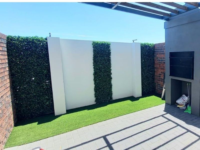 A well-maintained outdoor patio area featuring a built-in braai, pergola, paved flooring, and artificial turf, ideal for outdoor entertaining.
