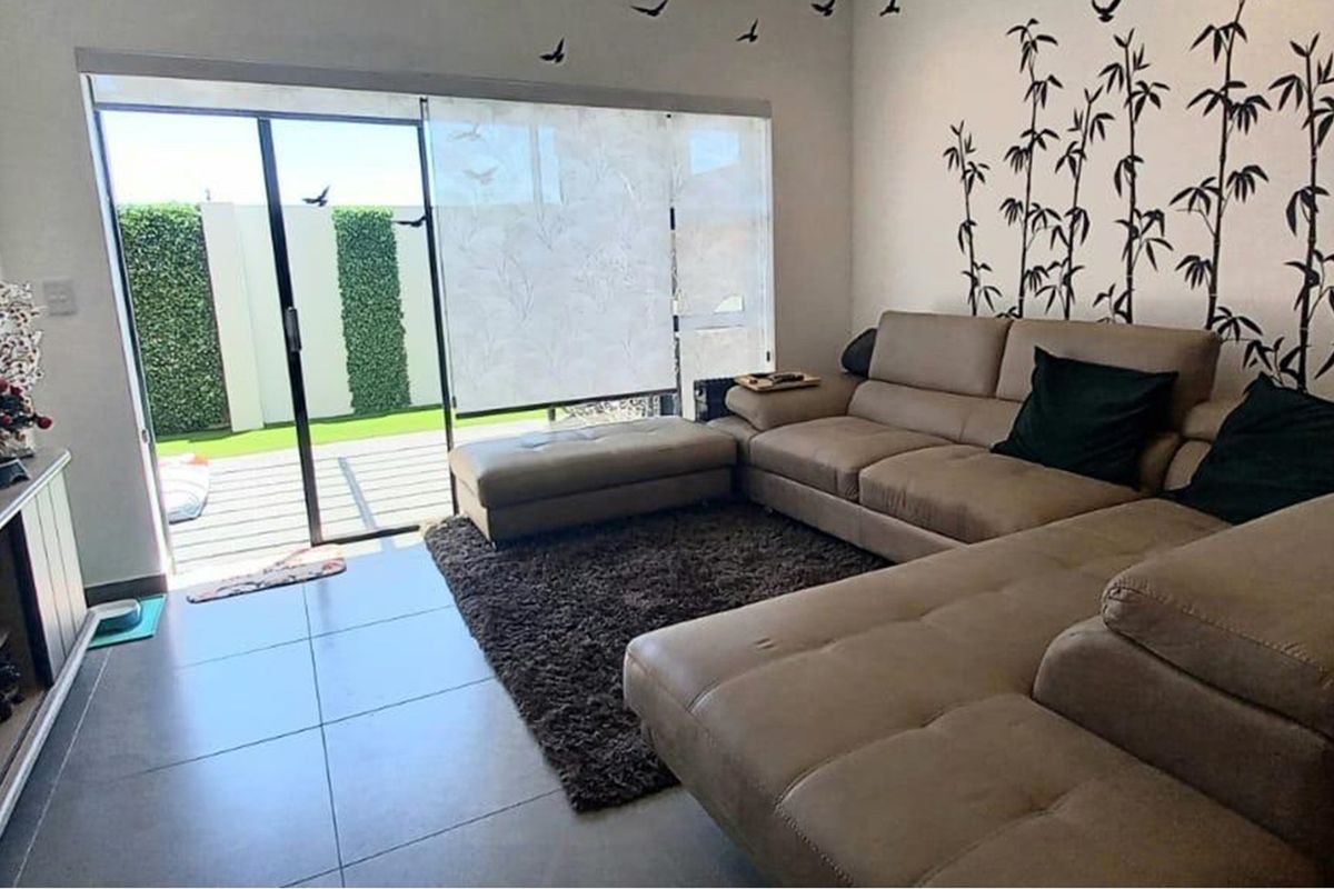 A bright living room featuring large sliding glass doors that open onto a patio area, complemented by neutral tiled flooring.