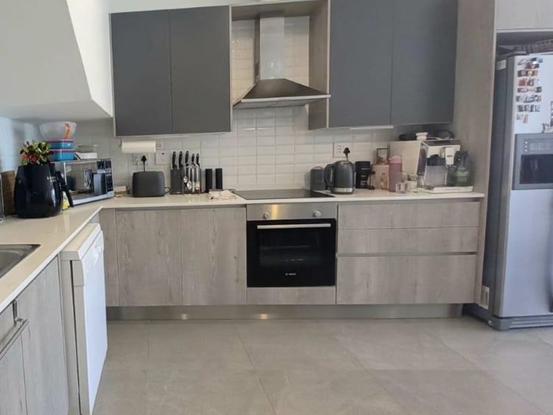 Modern kitchen featuring grey and wood-grain cabinetry, subway tile backsplash, stone countertops, and integrated stainless steel appliances.