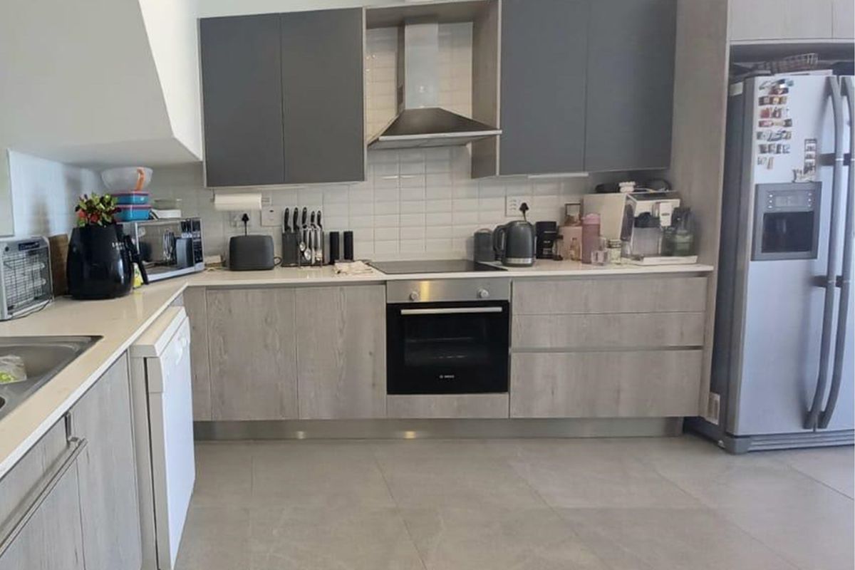 Modern kitchen featuring grey and wood-grain cabinetry, subway tile backsplash, stone countertops, and integrated stainless steel appliances.
