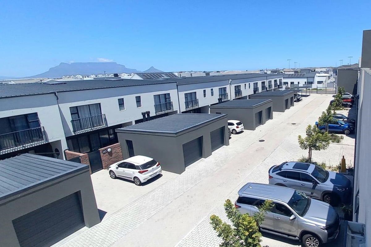 Aerial view of a modern townhouse complex featuring paved driveways, individual garages, and balconies with a scenic mountain backdrop.
