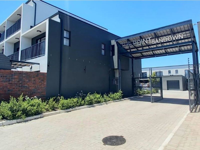 Front entrance view of The Point Sandown townhouse complex featuring a secure gated access point, paved driveway, and modern multi-story building facade.