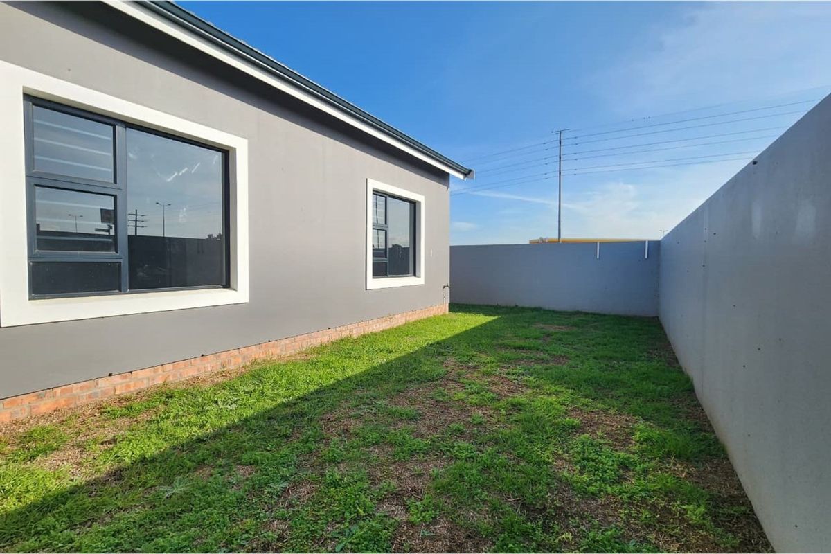 A view of the rear exterior of the house featuring a grey rendered facade, dark-framed windows, and a private enclosed garden area.