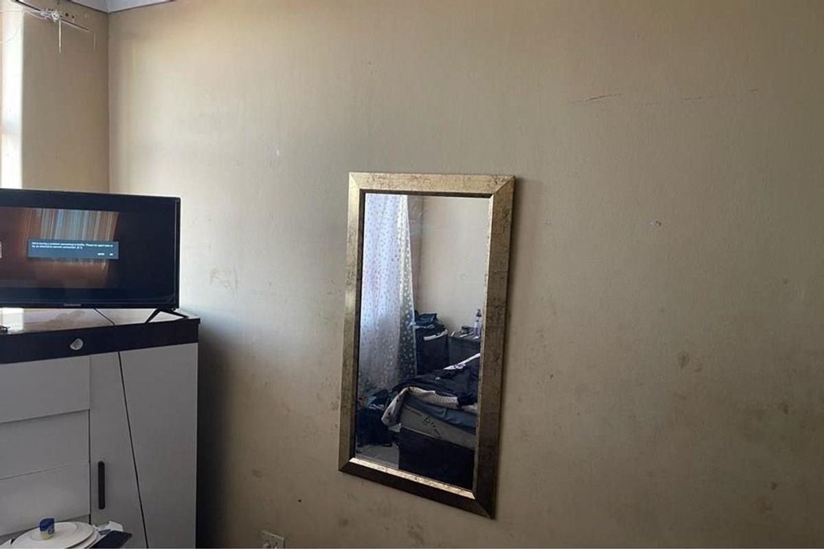 A bedroom interior featuring a plain wall surface with visible signs of wear and staining, requiring cosmetic attention.