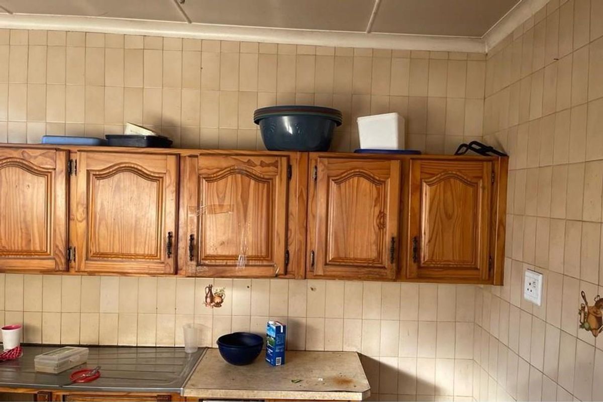 A dated kitchen area featuring traditional wooden cabinetry, tiled walls, and a stainless steel sink basin.