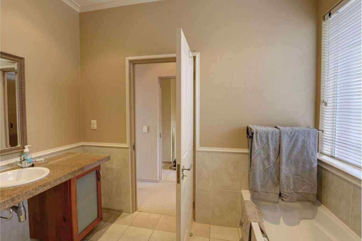 A functional bathroom featuring a vanity with a stone countertop, a bathtub with a window, and neutral tile wainscoting.