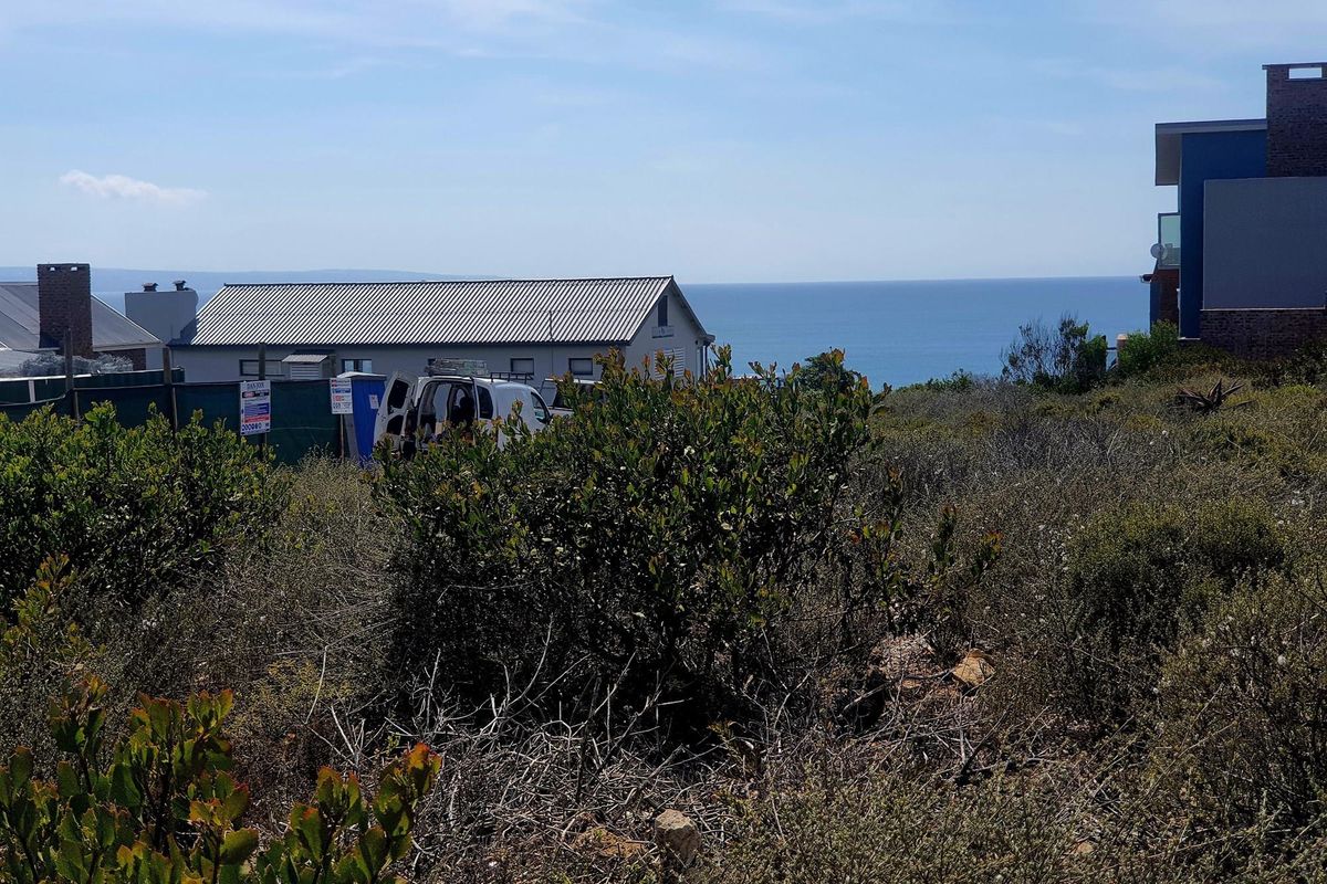 A view of a vacant residential plot featuring natural coastal vegetation with surrounding residential properties and a distant ocean view.