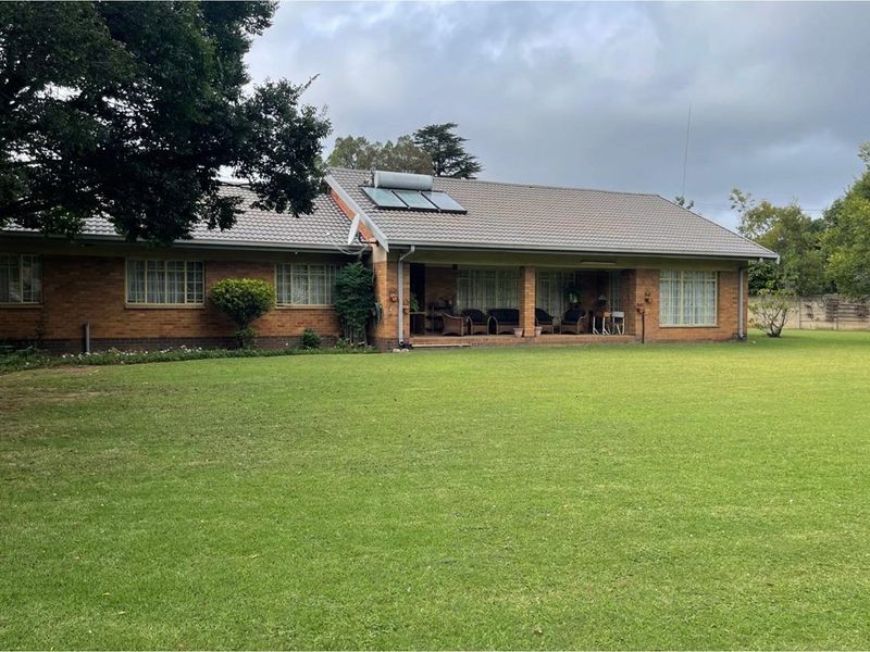 A rear view of a brick house featuring a covered patio area, tiled roof with solar water heating, and a spacious green lawn.