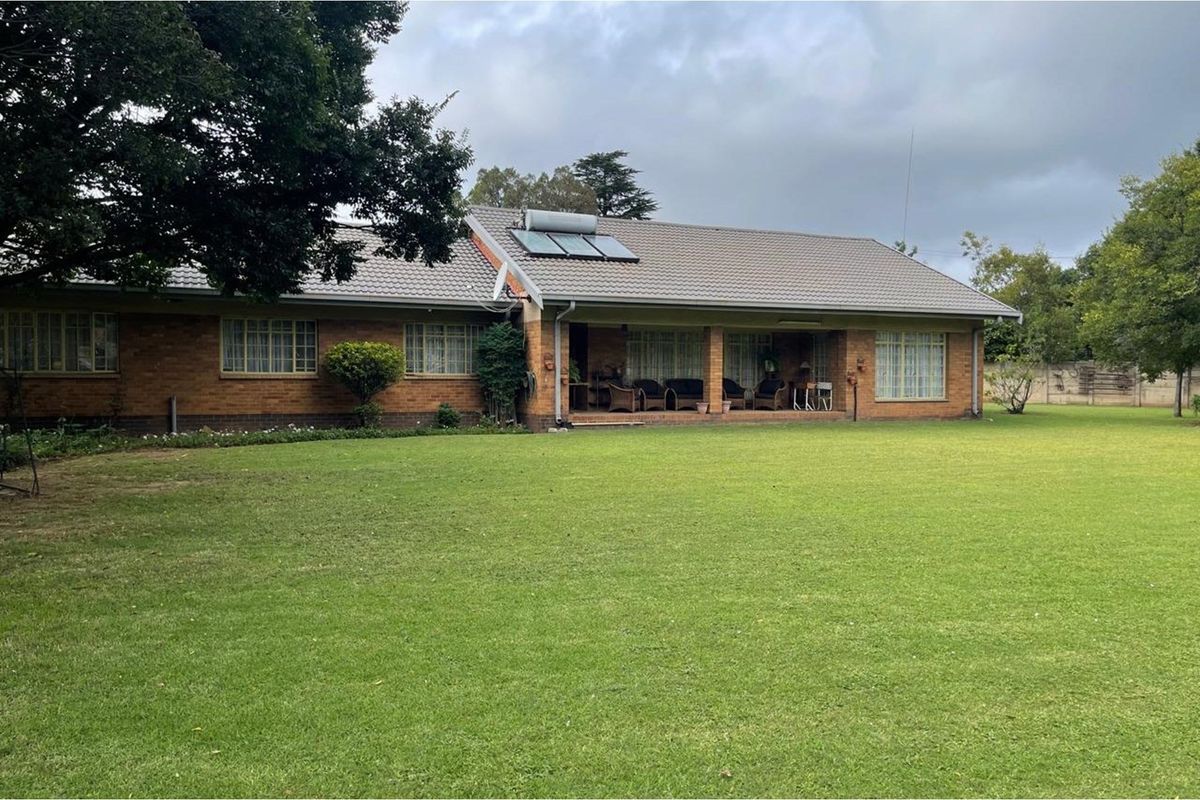 A rear view of a brick house featuring a covered patio area, tiled roof with solar water heating, and a spacious green lawn.