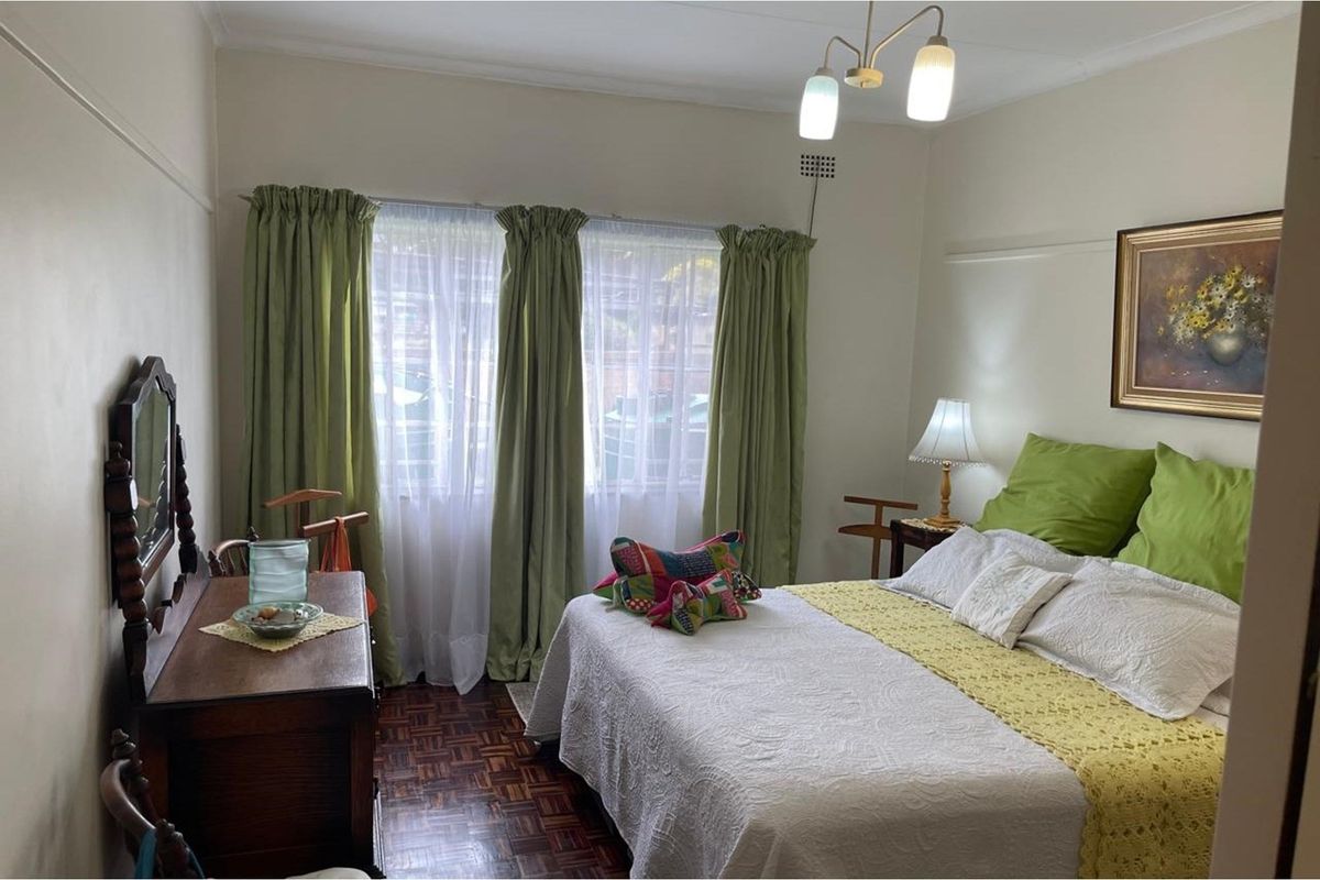 A well-maintained bedroom featuring classic parquet flooring, large windows with curtain tracks, and a central ceiling light fixture.