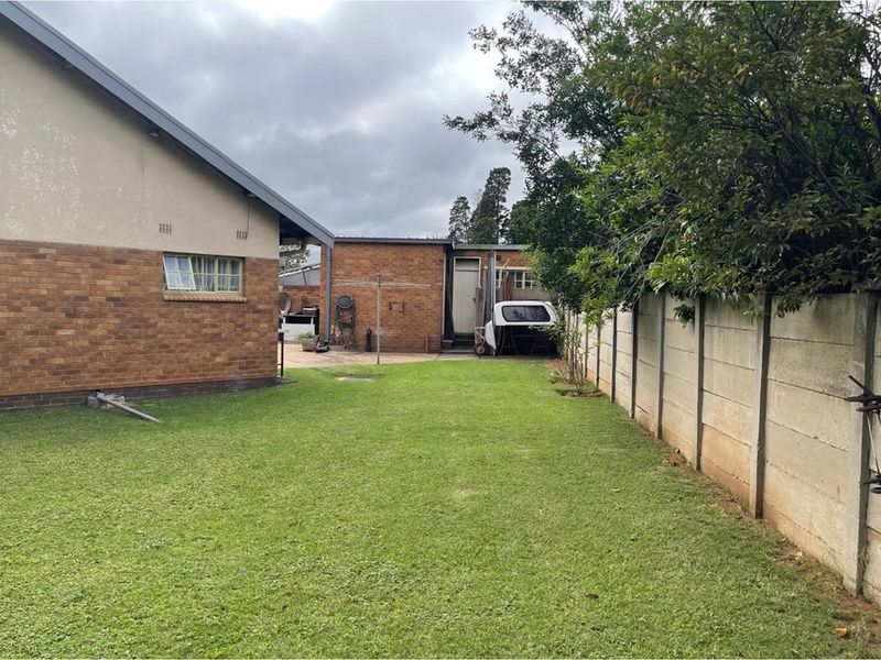 A spacious rear garden featuring a well-maintained lawn, enclosed by a concrete boundary wall, with access to the side of the house.