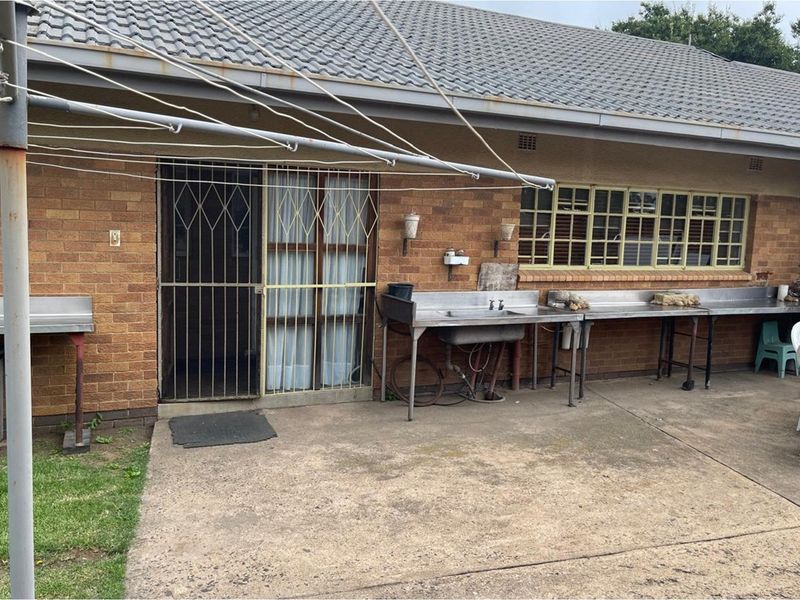 Rear exterior view of the house featuring a concrete patio area, brick facade, security gate, and outdoor stainless steel utility sink and prep counters.