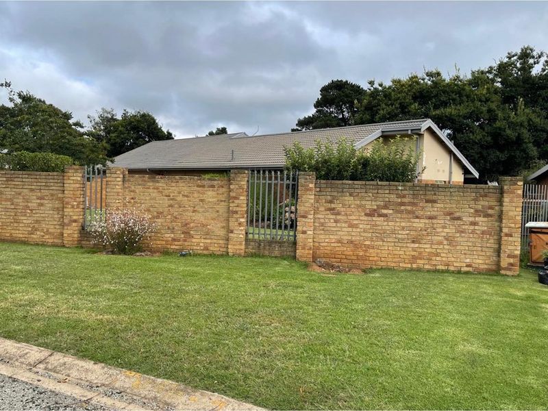 A street-facing view of the property featuring a brick boundary wall with integrated metal security gates and a tiled roof structure.